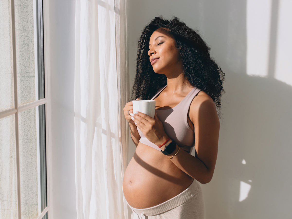 Schwangere Frau hält Tasse mit koffeinfreiem Kaffee in der Hand