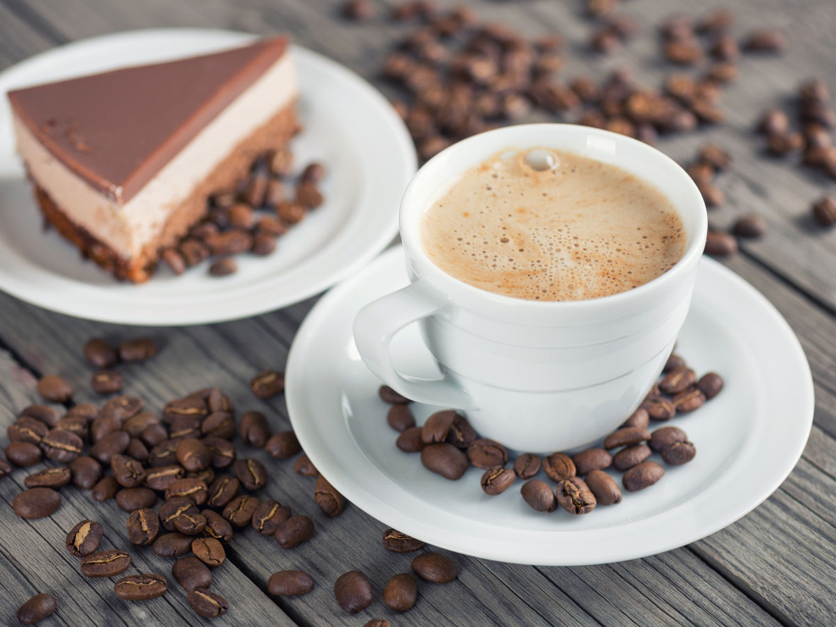 Fertig zubereiteter Verlängerter mit Kuchenstück im Hintergrund