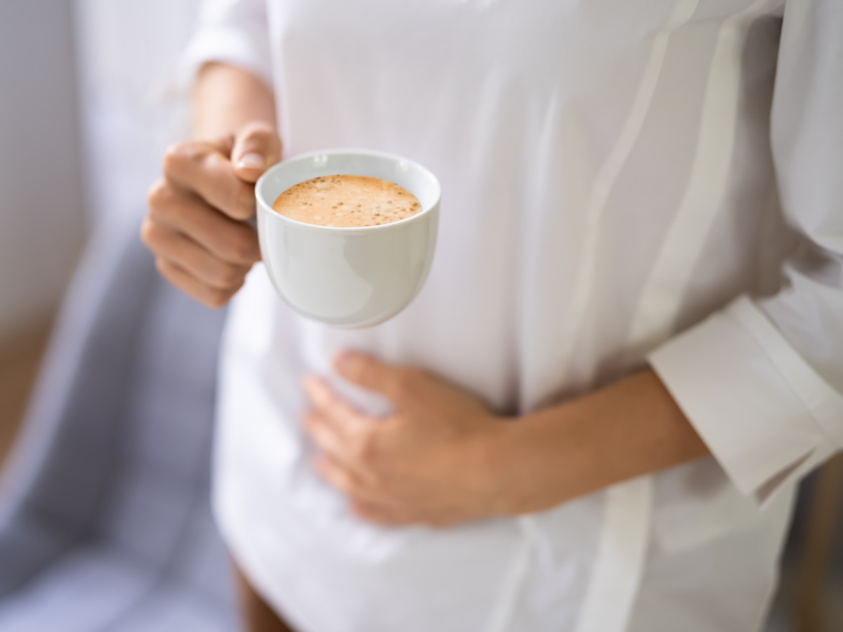 Person mit Kaffeetasse hat Bauchschmerzen wegen Kaffee-Unverträglichkeit